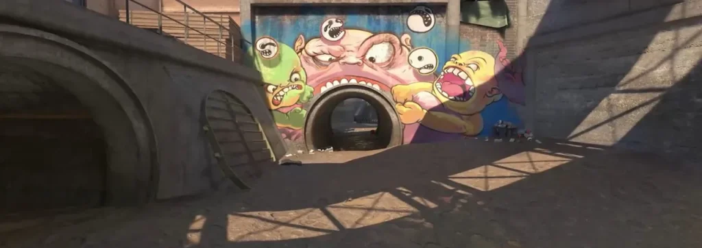 Bairro do mapa Overpass do CS2 com um grafite colorido de monstros em volta de um cano de concreto