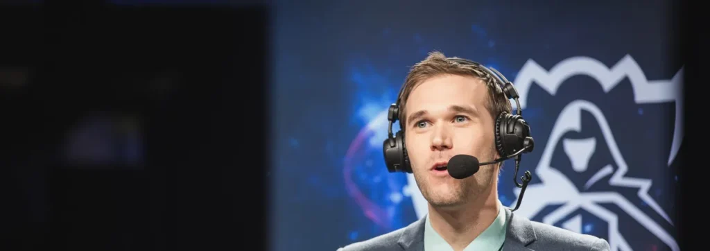 O narrador Kobe, de headset e microfone, comentando ao vivo diante do símbolo do Mundial de League of Legends