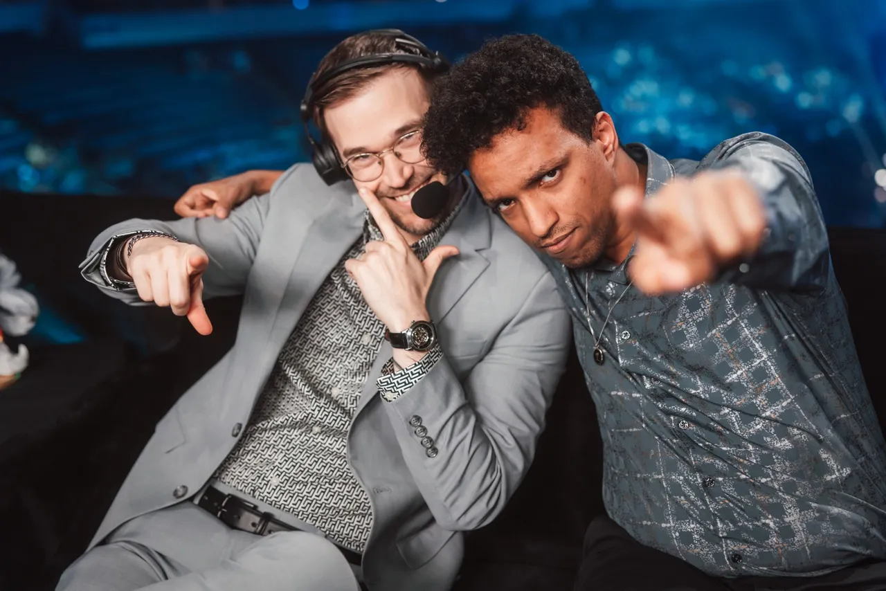Os casters Kobe e Raz, de headset, posam brincando na bancada da transmissão em inglês do Worlds 2026