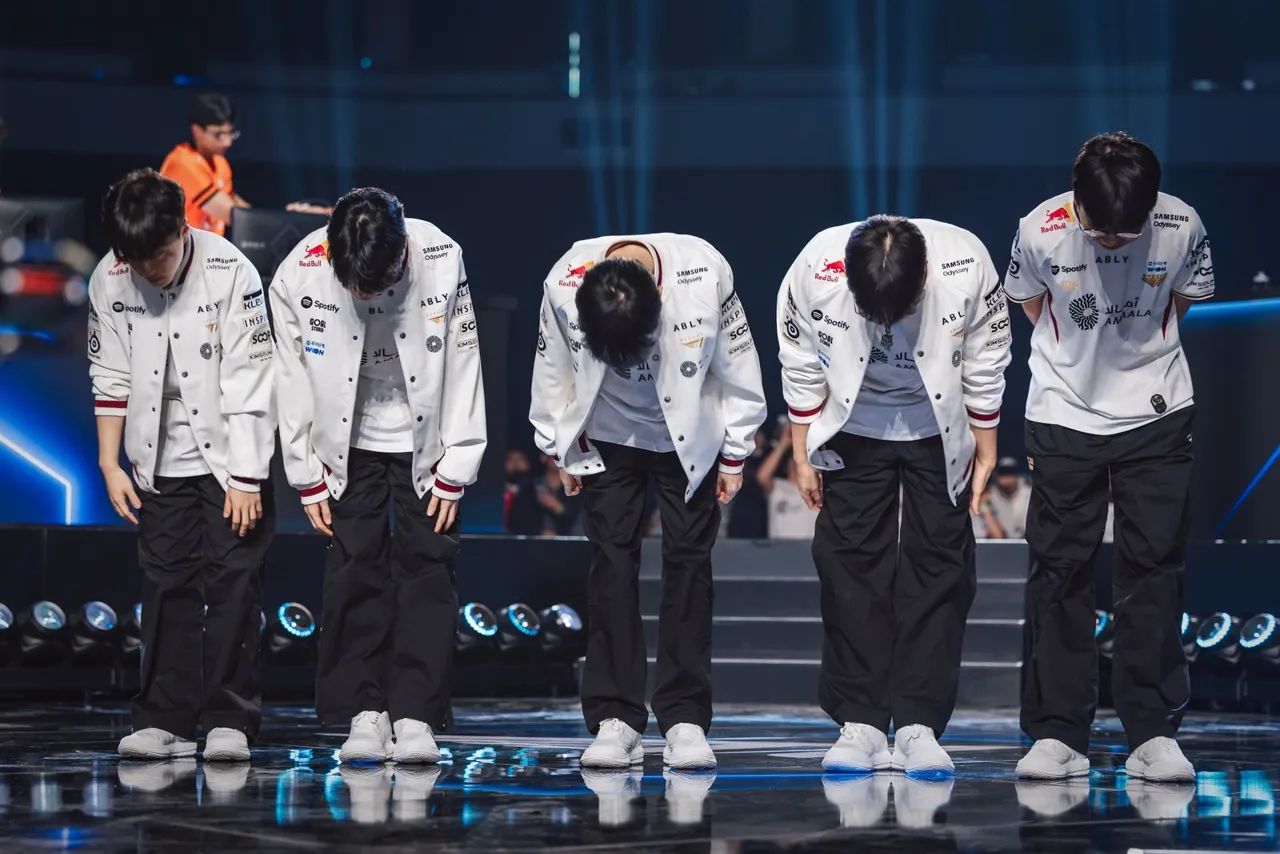 Os cinco jogadores da T1, de jaqueta branca, curvados em reverência para o público no palco do Worlds 2026